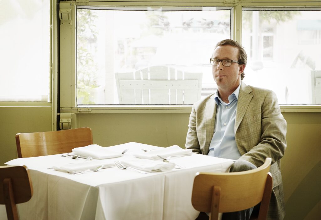 John T Edge sits at an empty dining table at Watershed Best