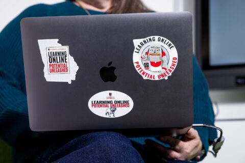 Detail of a laptop with branded stickers held by Amy Ragland, an instructional designer in the Office of Online Learning.