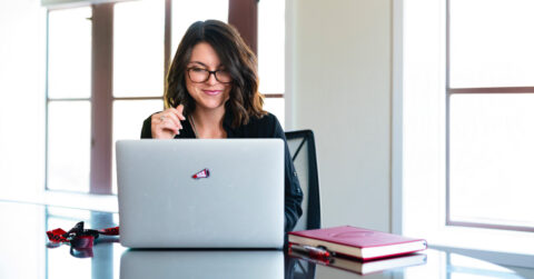 Adult woman student smiles at her laptop computer while surrounded by UGA swag