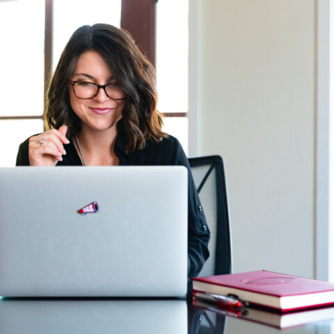 Adult woman student smiles at her laptop computer while surrounded by UGA swag
