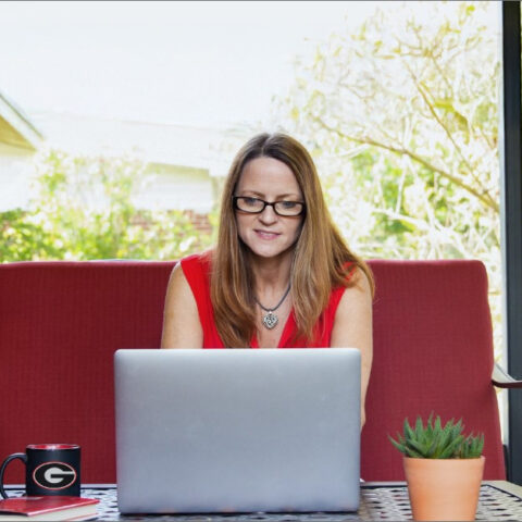 Woman with glasses studies at UGA in front of window